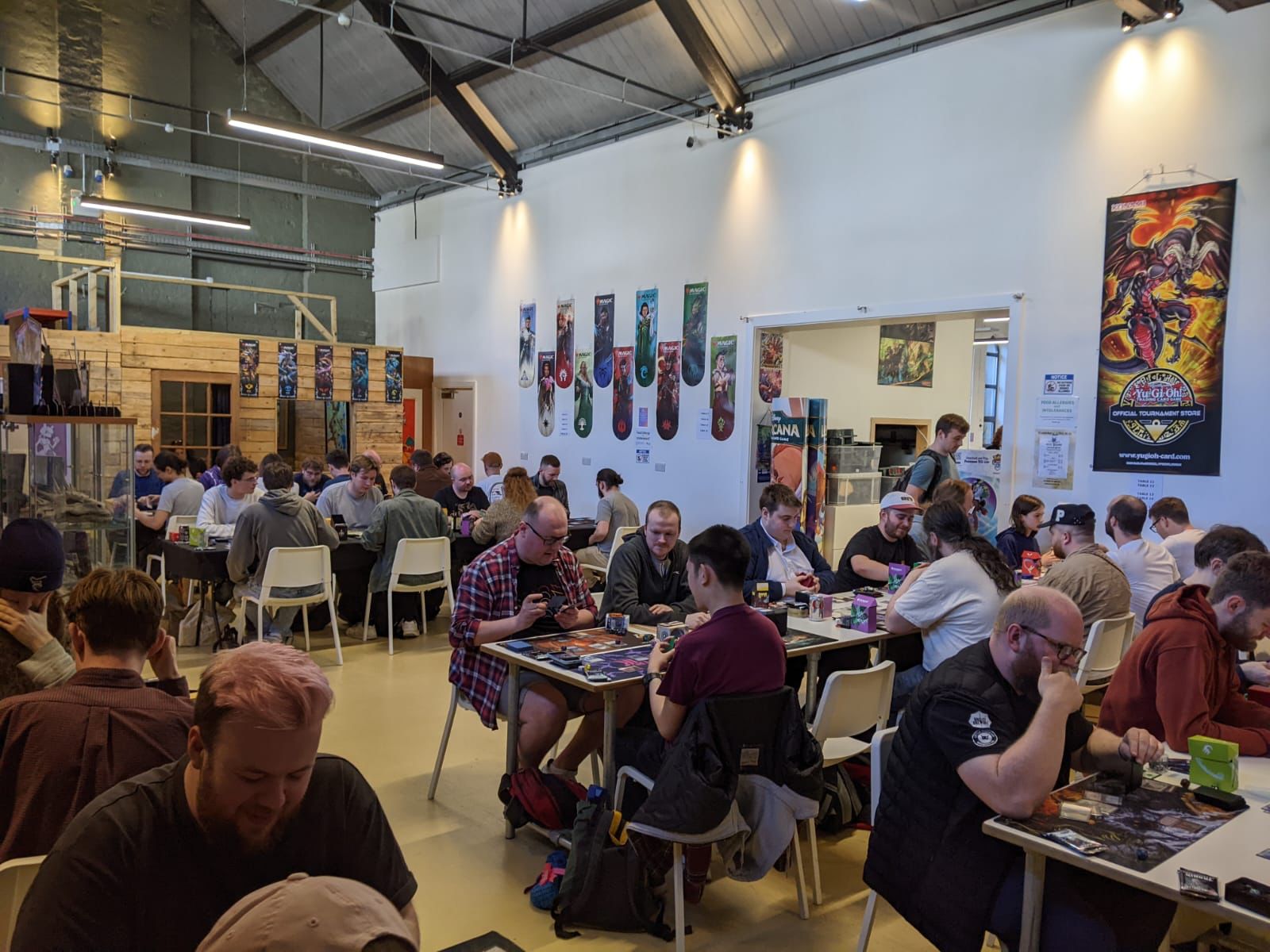 Group of people playing board games in a large indoor space with posters on the walls.