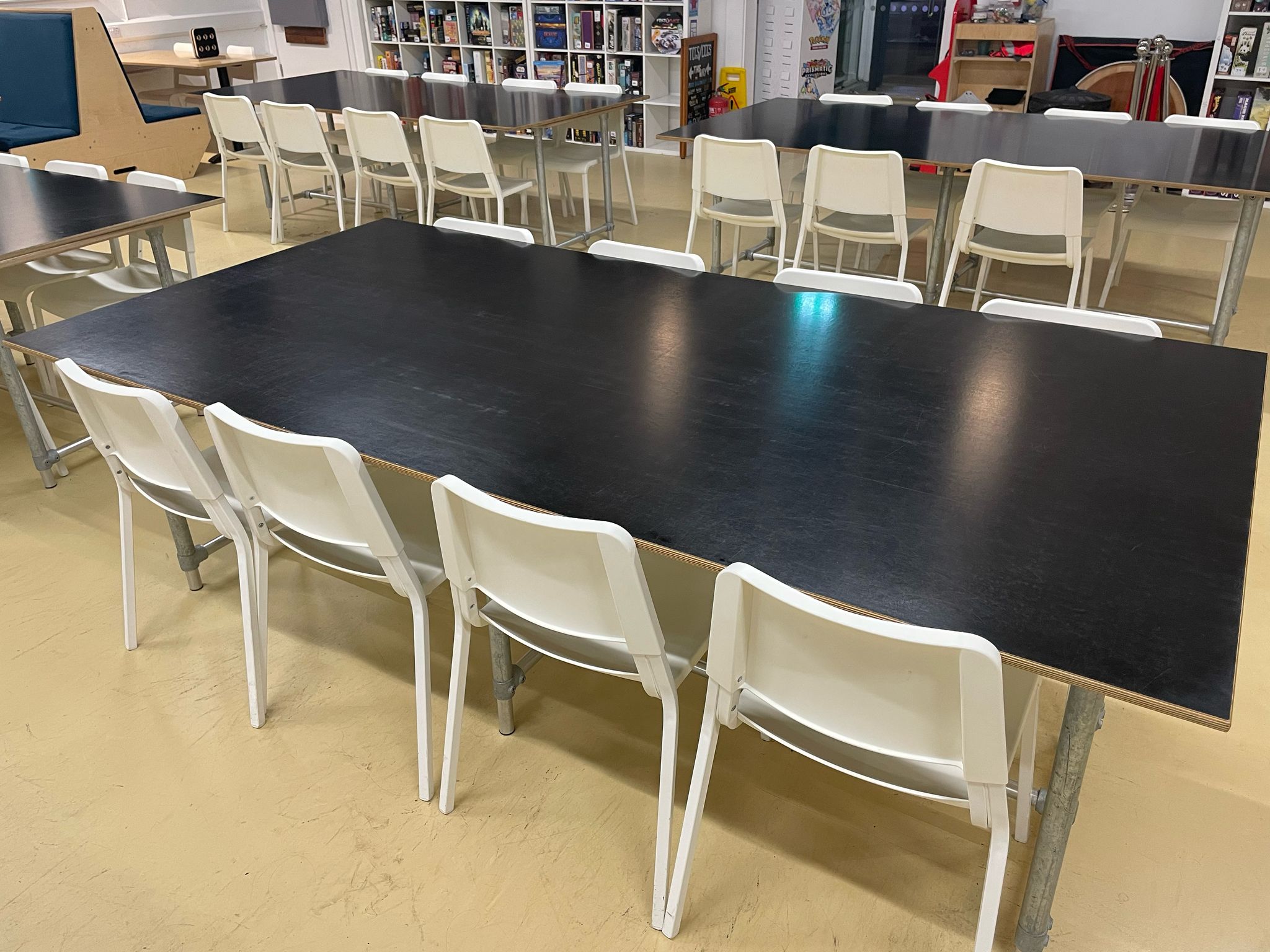Long black table with white chairs in a cafe setting